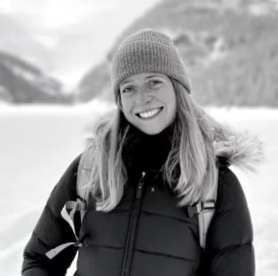 Ellie Riches smiling in a woolly hat and winter jacket, with snowy mountains behind her